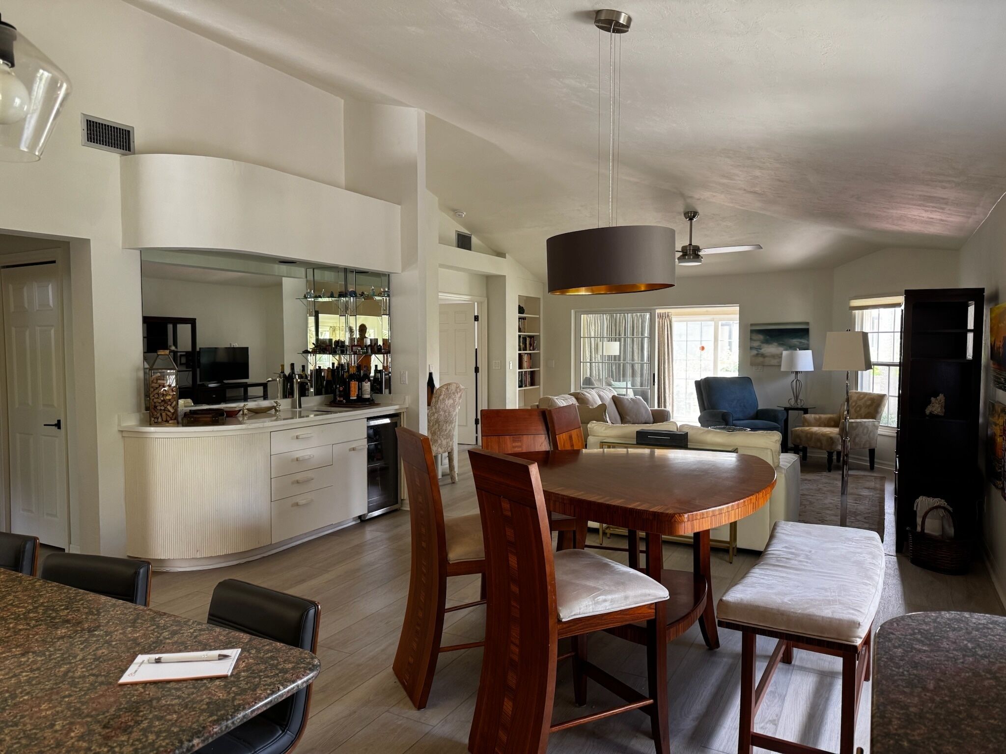 A modern kitchen with a dining area, a bar, and a living room with a sofa and chairs.