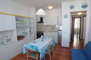 A compact kitchen with white cabinets, a microwave, and a dining table with chairs. - Residence Cala di Seta three-room apartment Luca with sea view for 5 people (Calasetta)