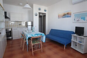 A compact living space with a kitchenette, dining area, and a sofa. - Residence Cala di Seta three-room apartment Luca with sea view for 5 people (Calasetta)