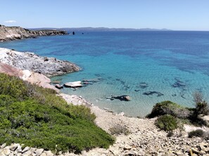 A coastal landscape with clear blue waters, rocky shores, and sparse vegetation. - Residence Cala di Seta three-room apartment Luca with sea view for 5 people (Calasetta)