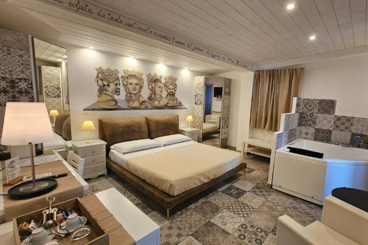 A hotel room with a bed, bedside tables, a desk, a chair, a bathtub, and a mirror.