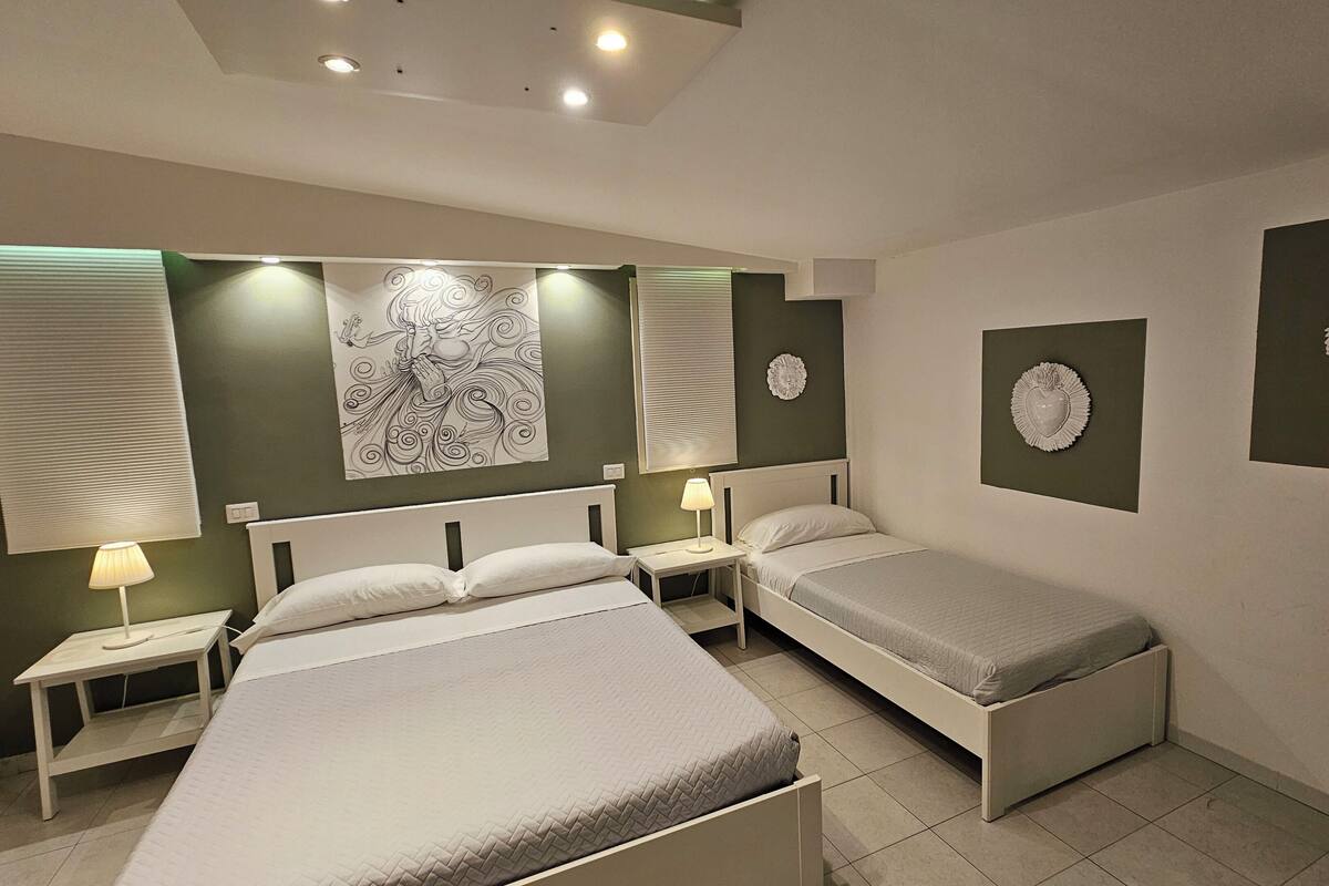 A bedroom with two beds, a nightstand, a wall-mounted lamp, and decorative wall art.