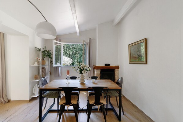 A dining room with a wooden table, chairs, a vase of flowers, a fireplace, and a painting on the wall.