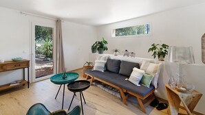 A modern living room with a sofa, a small table, and a window with plants. - Holiday Home 'Mer Et Montagne À Conca' with Mountain View, Private Terrace and Wi-Fi (Conca)
