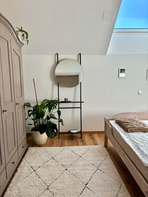 Une chambre à coucher avec un lit, une plante en pot, un miroir fixé au mur et une armoire en bois.