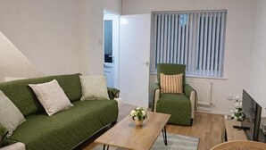 A living room with a green sofa, a wooden coffee table, a green armchair, and a window with blinds. - 2 Bed Home - Parking for 2, Wifi & Garden (Nottingham)