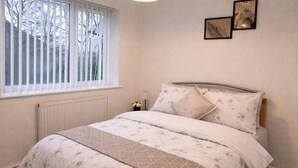 A bedroom with a bed, a radiator, a window with blinds, and two wall-mounted pictures. - 2 Bed Home - Parking for 2, Wifi & Garden (Nottingham)