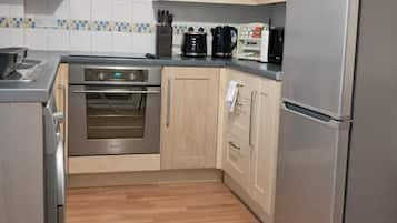 Una cocina con armarios de madera, un refrigerador de acero inoxidable, un horno empotrado y una cafetera.