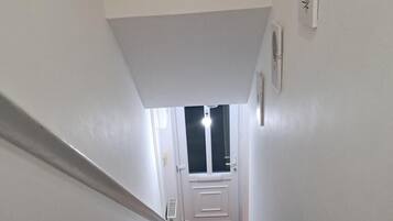 Una escalera conduce a una puerta con ventana, paredes blancas y una pequeña planta decorativa en la pared.