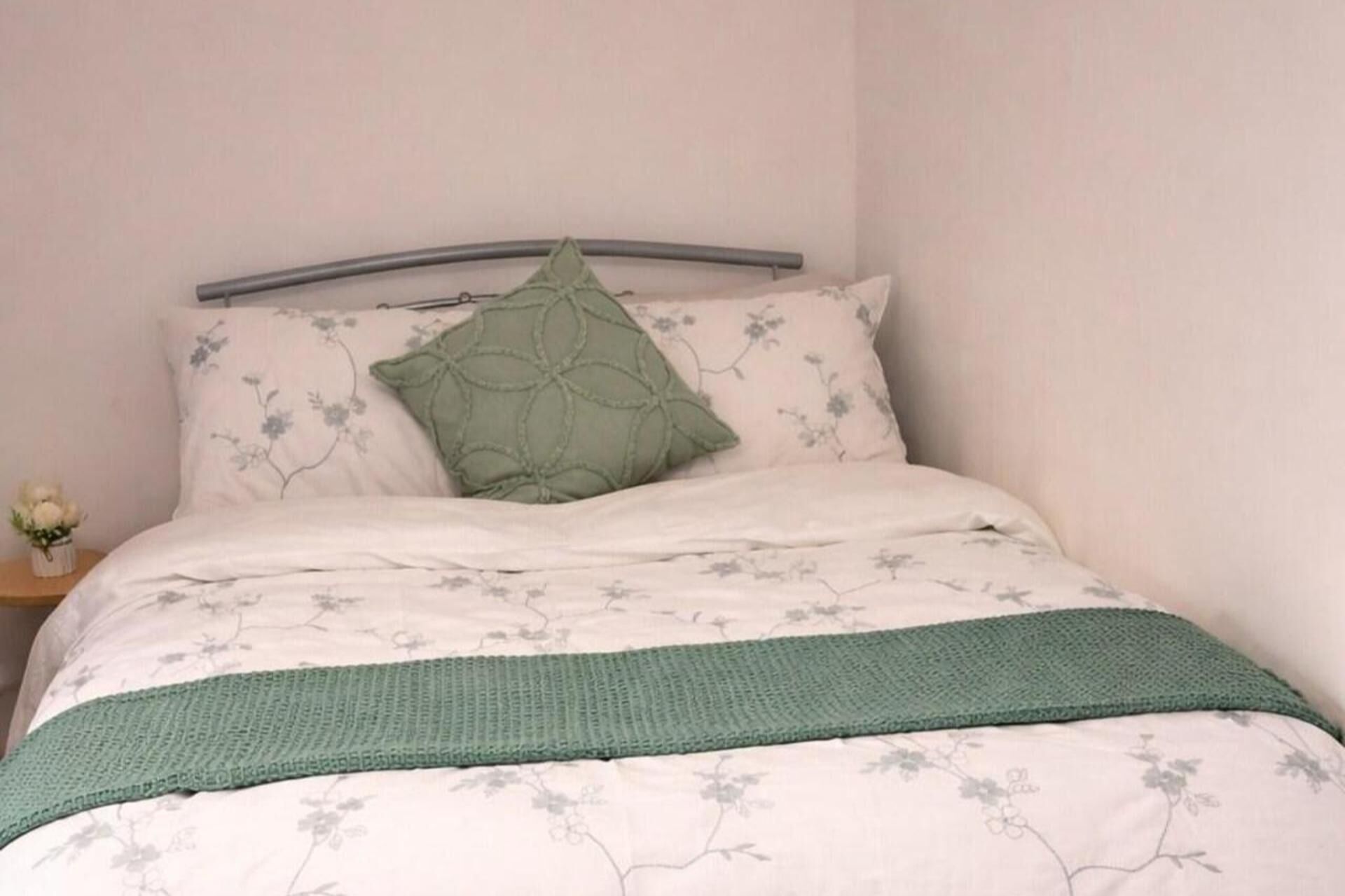 A bed with a floral-patterned bedspread, a green knitted throw, and a single green pillow.