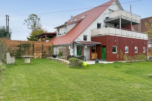 A two-story house with a sloped red roof, a balcony, and a green door. - Wiesenblick Apartment with Shared Terrace, Garden View, and Wi-Fi (Deggenhausertal)