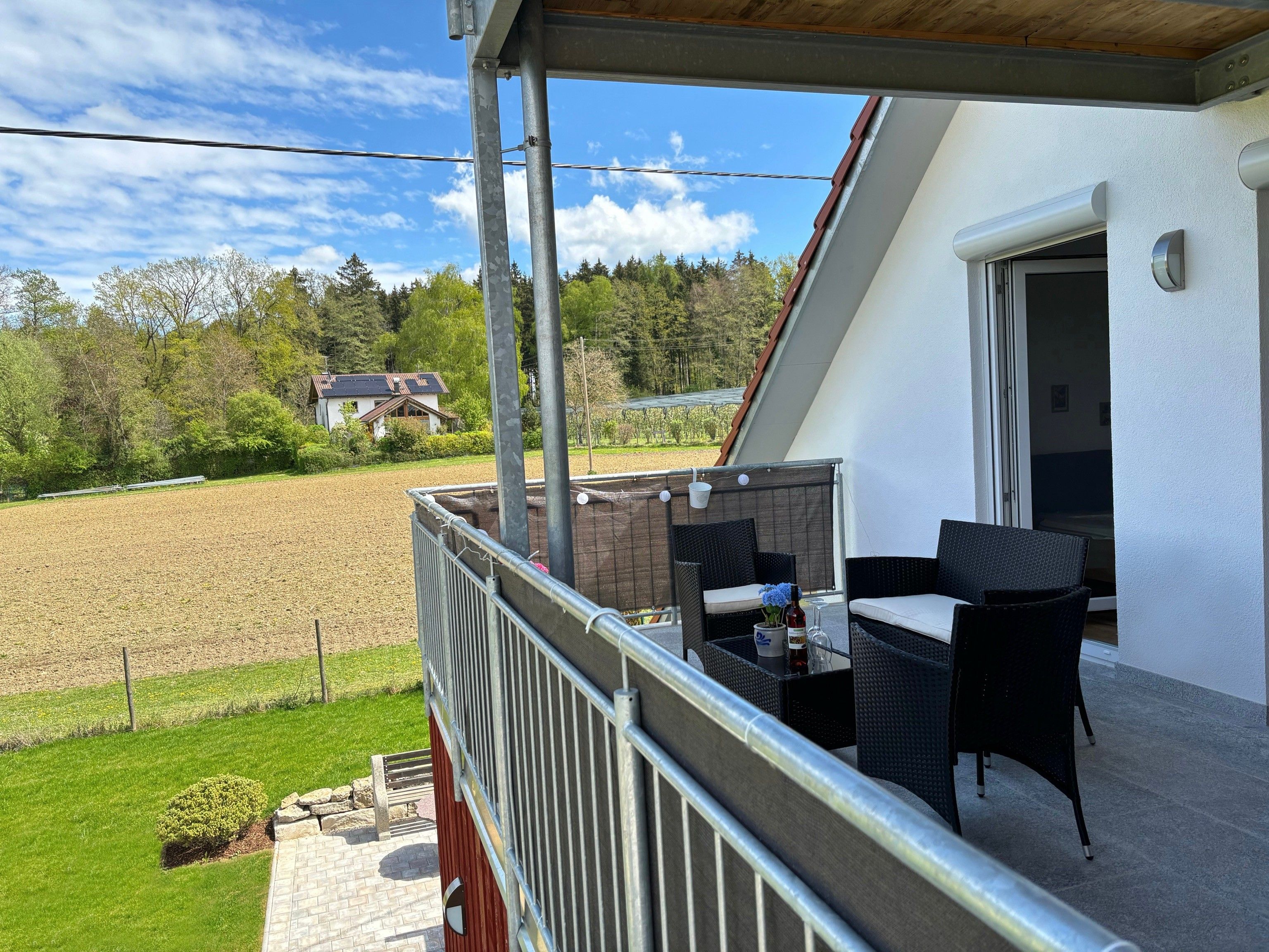 A balcony with outdoor furniture, a view of a field, and a building in the background.