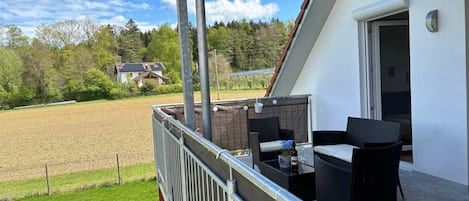 A balcony with outdoor furniture, a view of a field, and a building in the background.