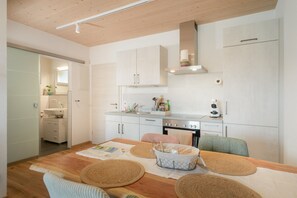 Une cuisine moderne avec des armoires blanches, une cuisinière en acier inoxydable et un coin repas comprenant une table et des chaises en bois.