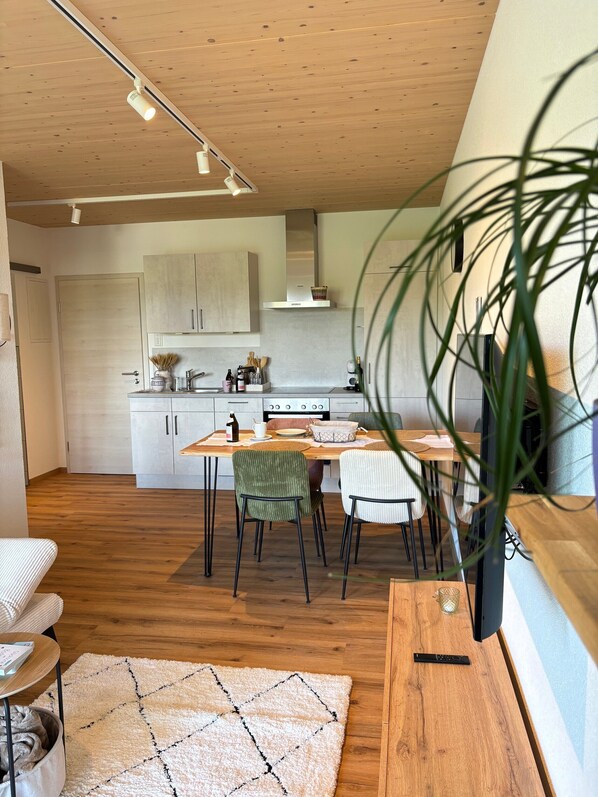 Een moderne keuken met houten kastjes, een eettafel met stoelen, een televisie en een plant.