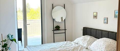 A bedroom with a bed, a bedside plant, a mirror, and a view through a door.