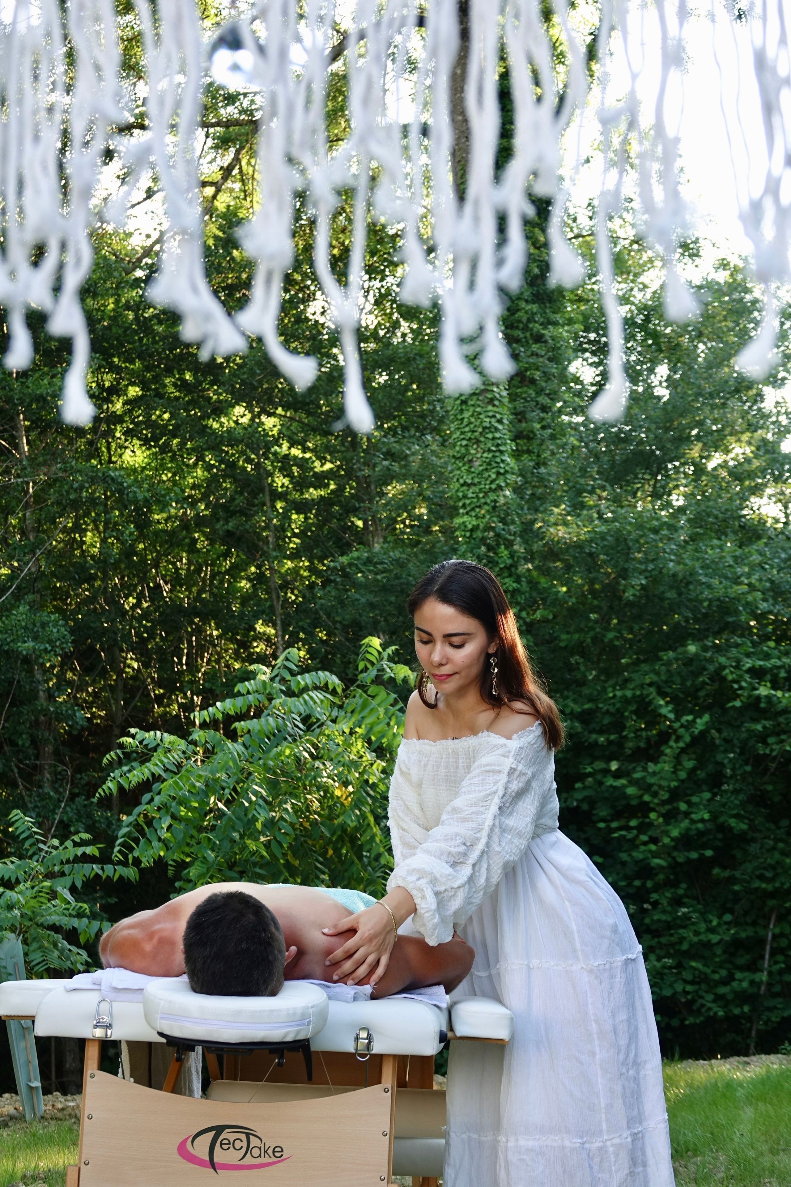 A massage therapy session taking place outdoors with a wooden massage table and a person receiving a back massage.