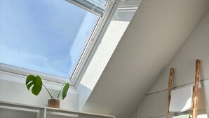 A modern bathroom with a skylight, white shelves with towels, a wooden ladder, and a potted plant. - Panoramic View Holiday Apartment (Deggenhausertal)