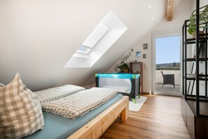 Een slaapkamer met een schuine kap, een bed met geruit beddengoed, een dakraam, een klein bureau en uitzicht op de omgeving.