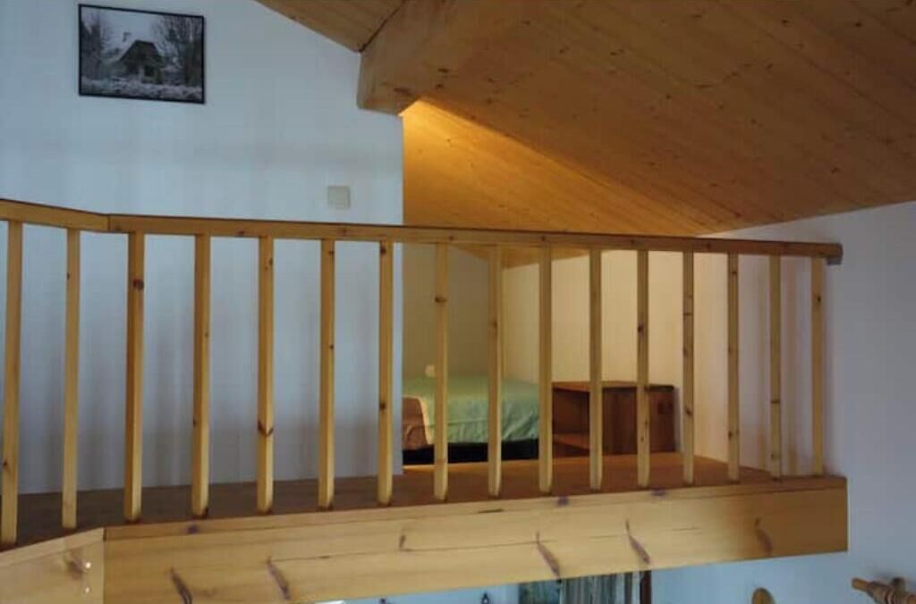 Une chambre avec un balcon en bois, un lit et une petite fenêtre.