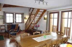 Un espace repas comprenant une table en bois, des chaises, un escalier et de grandes fenêtres.