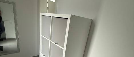 Una habitación con una estantería blanca adosada a una pared, una puerta y una ventana.
