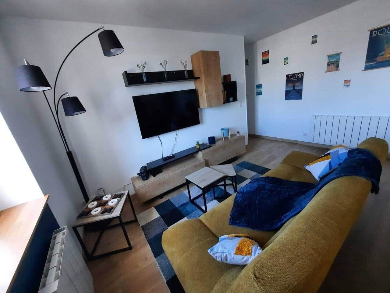 A living room with a sofa, a coffee table, a TV mounted on the wall, a floor lamp, and a small table with a tray.