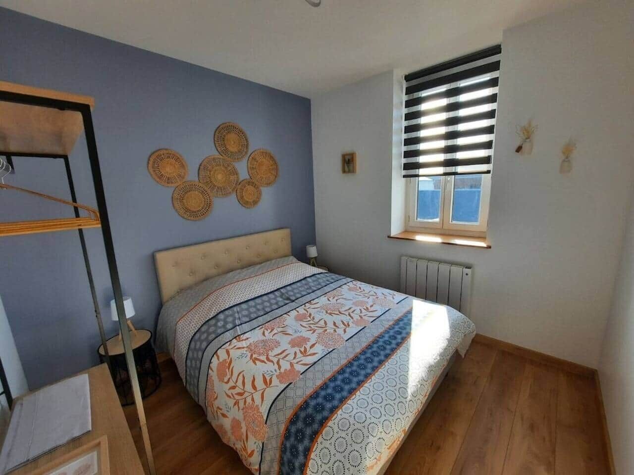 A bedroom with a bed, a window with blinds, a radiator, and wall decor.