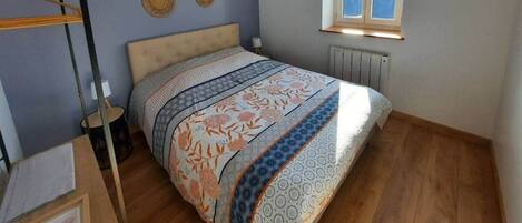A bedroom with a bed, a window with blinds, a radiator, and wall decor.