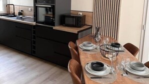 A modern kitchen with a microwave, oven, and sink. There is a dining table set with plates and glasses. - Duplex Chic et Confort (Fécamp)