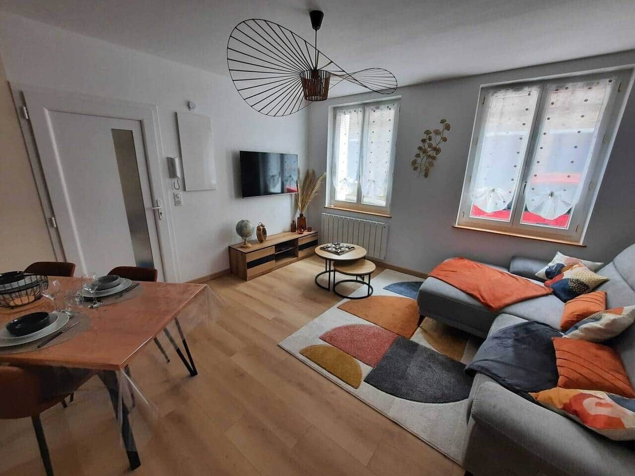 A modern living room with a dining area, a sofa set, a TV, and a window with curtains.