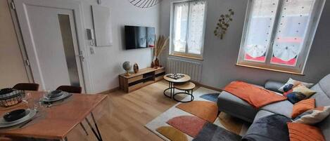 A modern living room with a dining area, a sofa set, a TV, and a window with curtains.