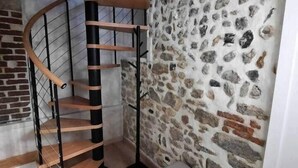 A spiral staircase with wooden steps and metal railings, a stone wall, and a bench. - Duplex Chic et Confort (Fécamp)