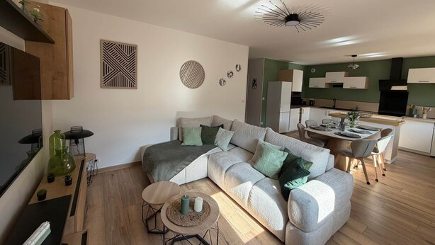 Uma sala de estar moderna com sofá de canto, mesa de jantar e cozinha ao fundo.