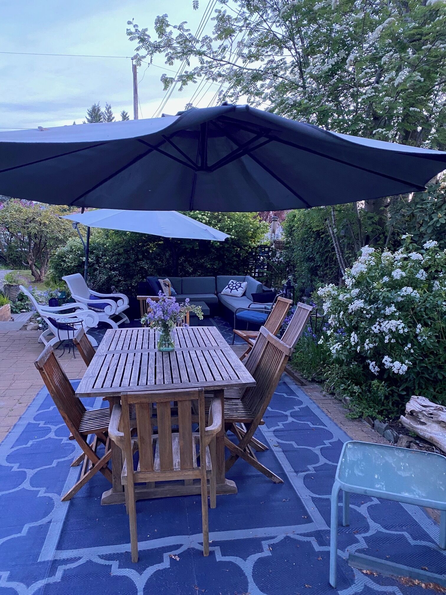 An outdoor patio with a wooden table and chairs, a large umbrella, and a blue patterned floor.