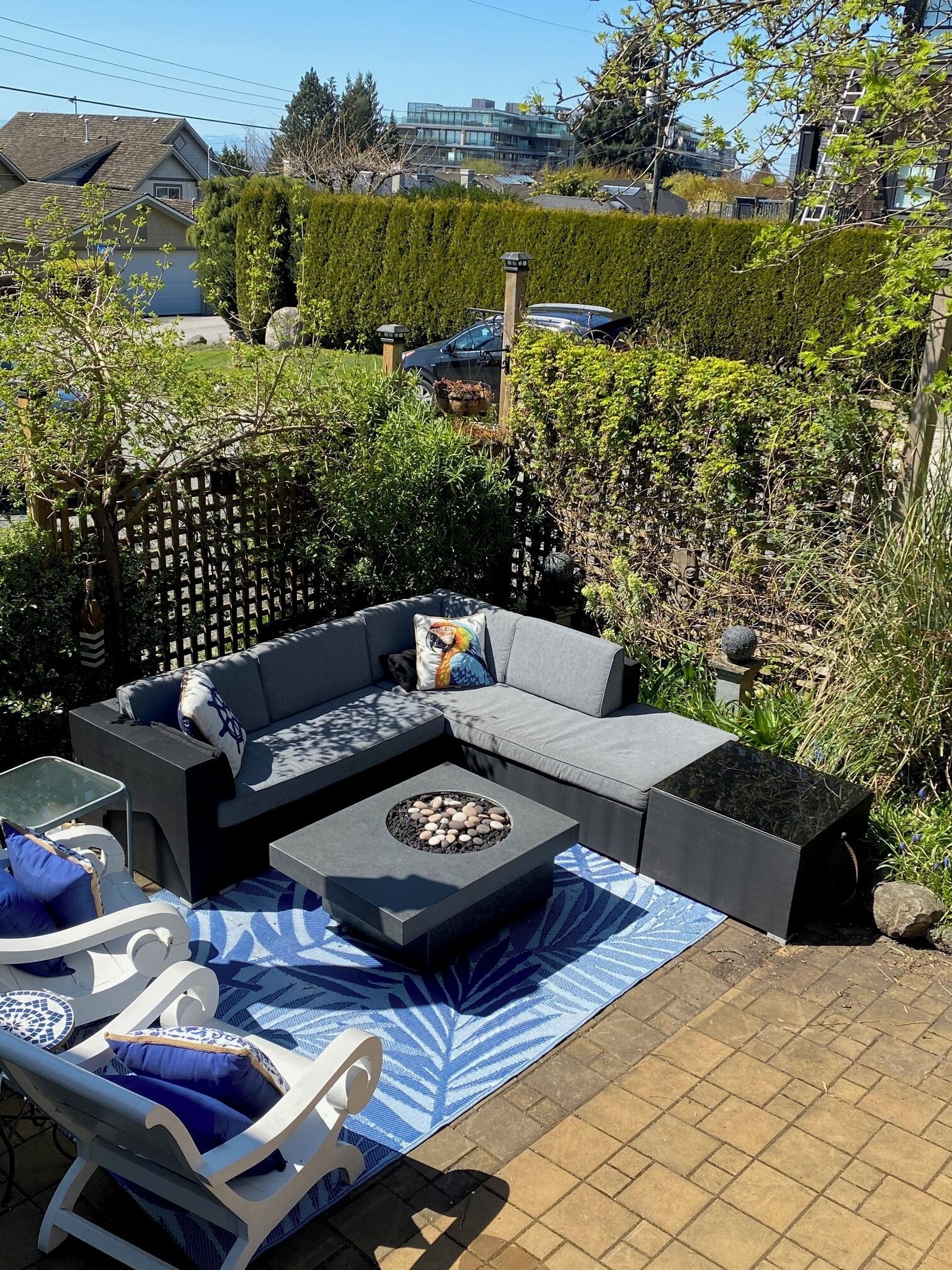 A patio with a grey sofa, a round table, and a blue patterned rug.