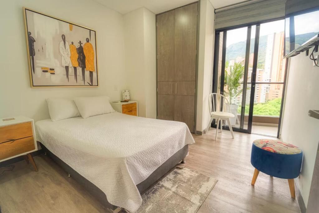 A bedroom with a bed, a nightstand, a chair, a window with a view, and a wardrobe.