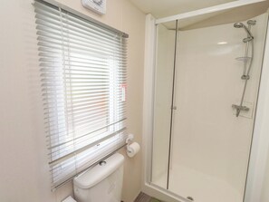 Une salle de bain comprenant des toilettes, une douche avec une porte en verre et une fenêtre avec des stores.