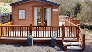 A wooden lodge with a wooden deck, two potted plants, and a sign reading 'Gardeners Lodge.' - Gardeners Lodge (Belford)