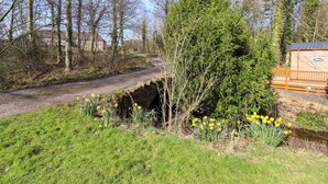 A rural landscape with a dirt path, a stone bridge, and a wooden building. - Gardeners Lodge (Belford)
