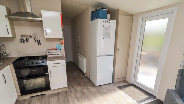 A compact kitchen with a stove, oven, white cabinets, and a refrigerator. - Gardeners Lodge (Belford)