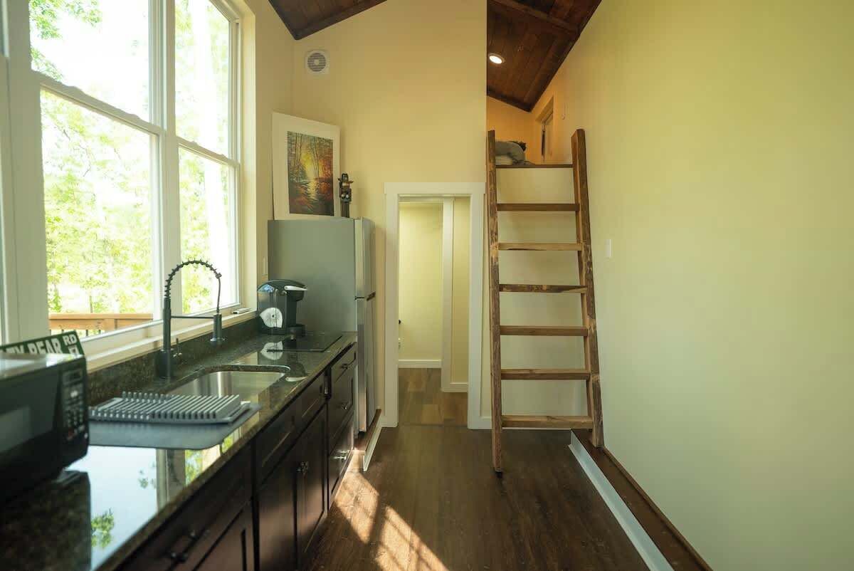 A kitchen with a large window, a ladder, and a door leading to another room.