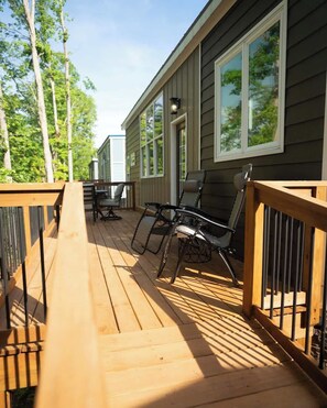 Um deck de madeira com móveis de exterior, guarda-corpo e um edifício com grandes janelas.