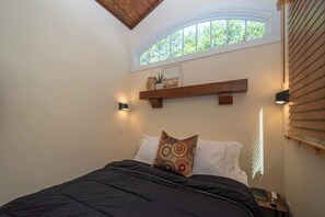 Ein Schlafzimmer mit Bett, Fenster, Regal und Nachttisch.