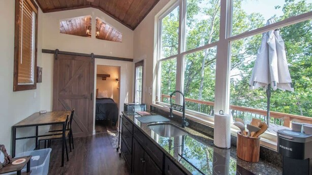 A kitchen with a large window, a wooden ceiling, and a view of trees. - Saddle (Anderson)