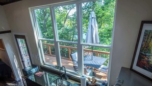 A kitchen with a large window, a deck, and a view of trees. - Saddle (Anderson)