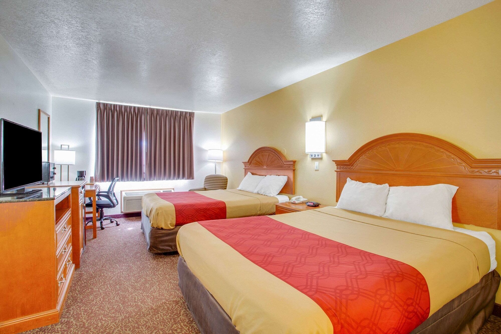 A hotel room with two beds, a desk with a TV, a chair, a lamp, and a window with curtains.