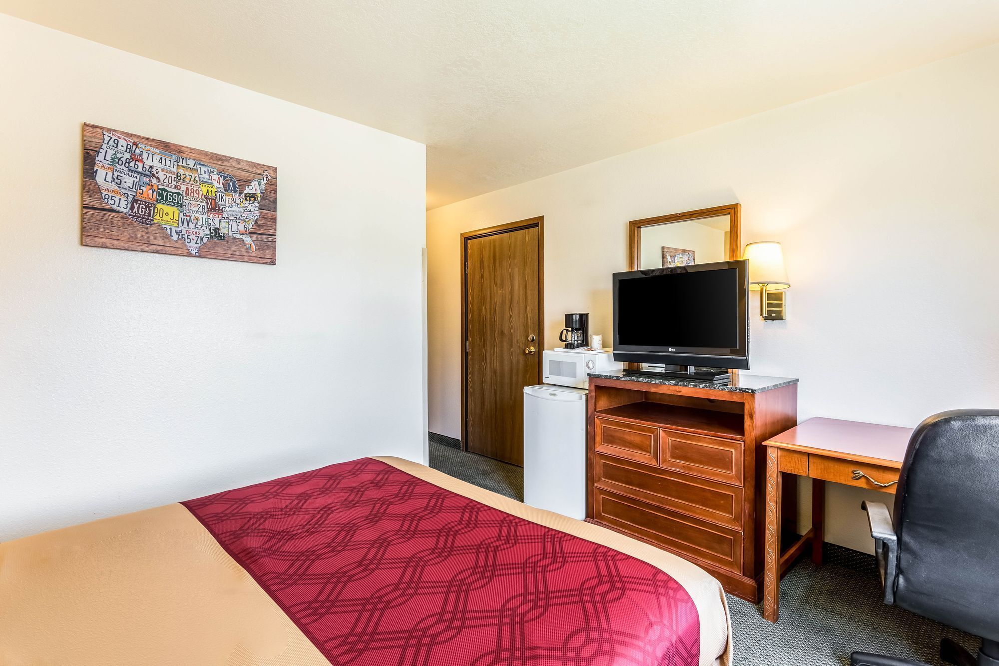 A hotel room with a bed, a desk, a television, a microwave, and a refrigerator.