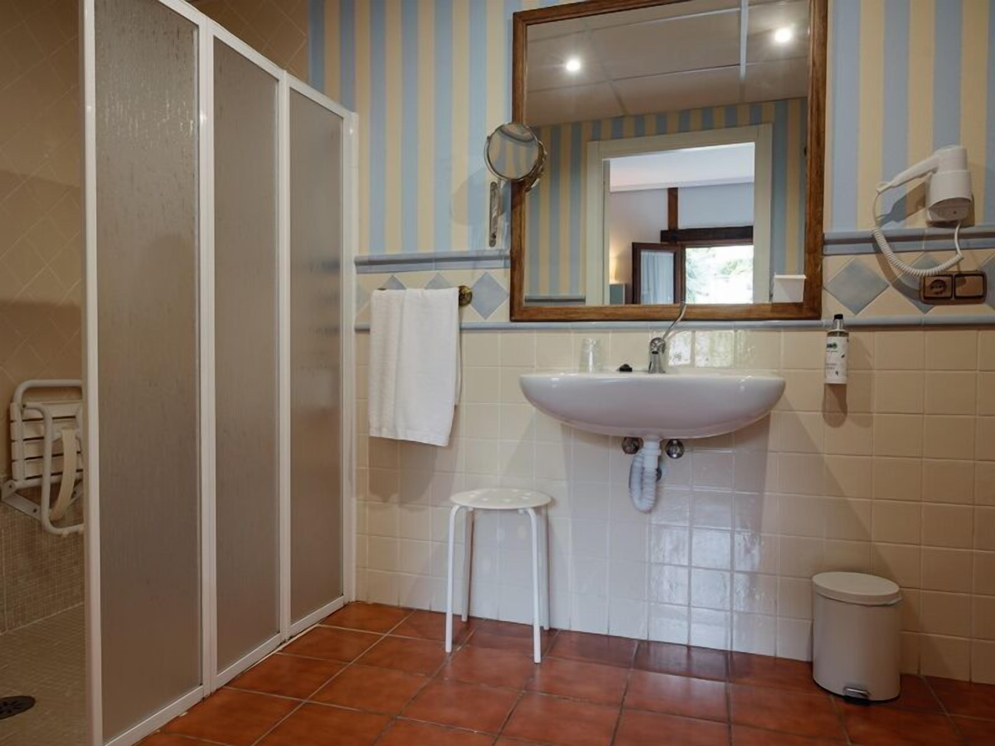 Un baño con ducha, lavabo, espejo y toallero.
