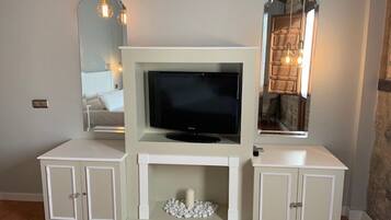 Una habitación con televisor sobre un mueble blanco, una chimenea de piedras blancas y dos aparadores a los lados.